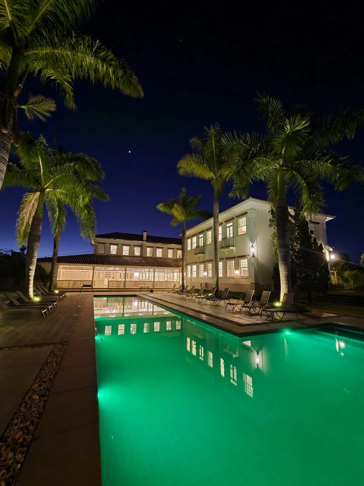 Piscina iluminada à noite entre palmeiras